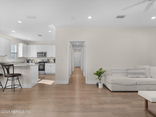 kitchen with white cabinets, appliances with stainless steel finishes, light hardwood / wood-style flooring, and a kitchen breakfast bar