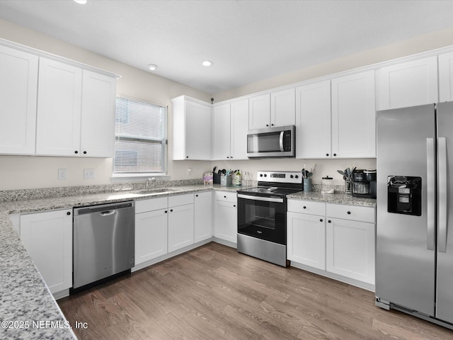 kitchen featuring light stone countertops, white cabinetry, stainless steel appliances, and light hardwood / wood-style flooring