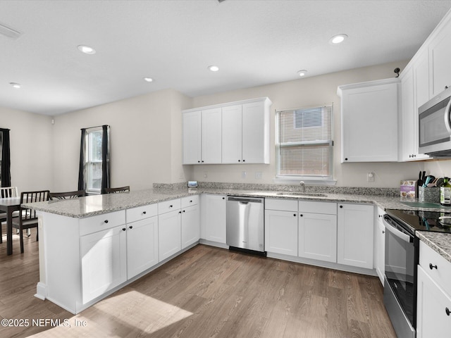 kitchen featuring kitchen peninsula, stainless steel appliances, sink, light hardwood / wood-style flooring, and white cabinets