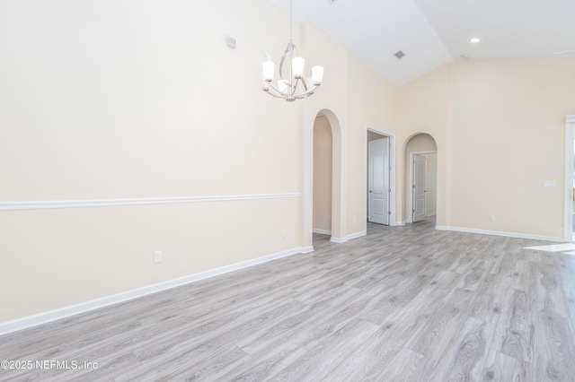 spare room featuring high vaulted ceiling, light hardwood / wood-style flooring, and a notable chandelier