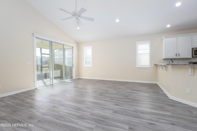 unfurnished living room with ceiling fan, light hardwood / wood-style floors, and vaulted ceiling