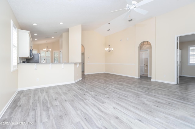 unfurnished living room featuring high vaulted ceiling, ceiling fan with notable chandelier, and light hardwood / wood-style flooring