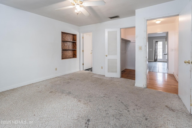 unfurnished bedroom featuring ceiling fan, a walk in closet, a closet, and light carpet