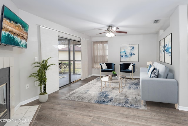 living room with ceiling fan, wood-type flooring, and a tiled fireplace