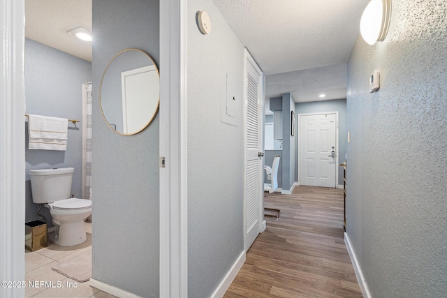 hallway with a textured ceiling and light hardwood / wood-style flooring