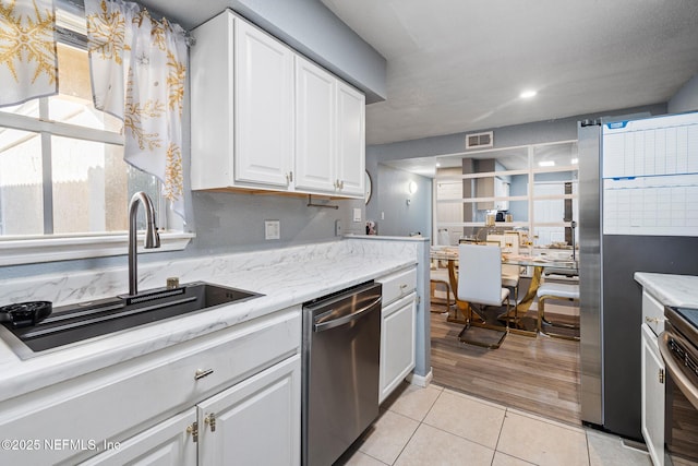 kitchen featuring dishwasher, white cabinets, light tile patterned flooring, and sink