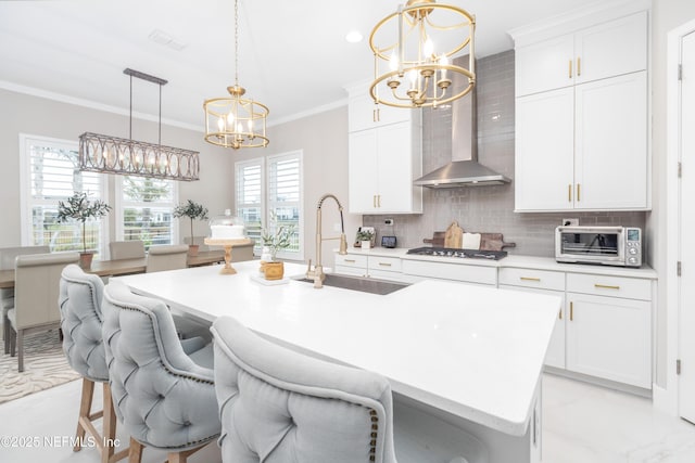 kitchen featuring wall chimney exhaust hood, a kitchen island with sink, backsplash, white cabinets, and sink