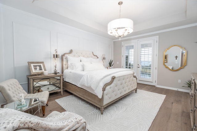 bedroom with a raised ceiling, a notable chandelier, access to exterior, and hardwood / wood-style floors