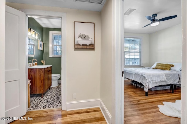 bedroom with light wood-type flooring, ensuite bathroom, ceiling fan, and sink