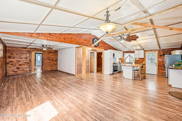 unfurnished living room with vaulted ceiling, ceiling fan, wooden walls, and light hardwood / wood-style flooring