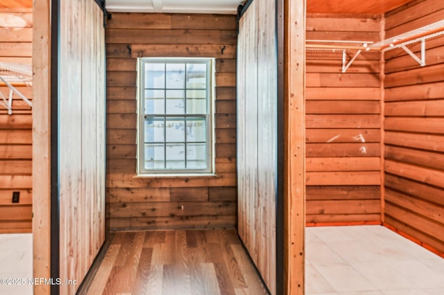 corridor with a barn door, wooden walls, and hardwood / wood-style flooring