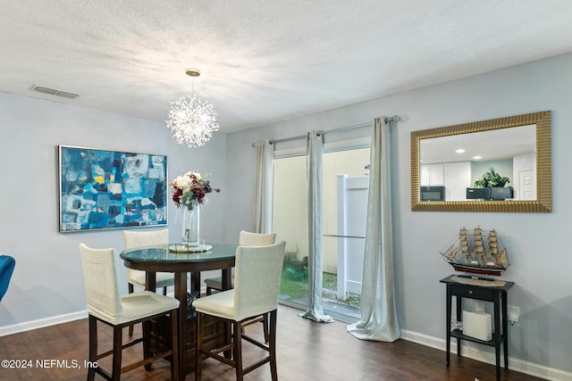 dining area with a textured ceiling, a notable chandelier, and dark wood-type flooring