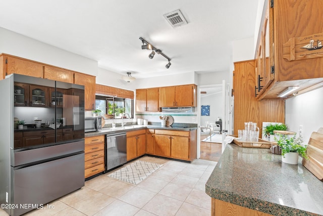 kitchen featuring dark stone counters, sink, light tile patterned floors, and stainless steel appliances