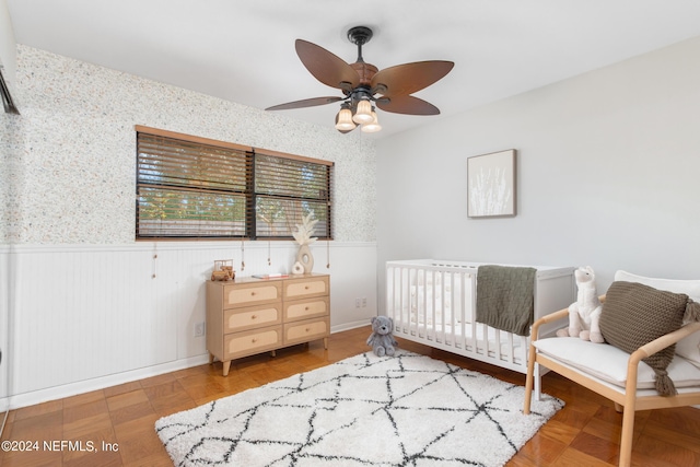 bedroom with a crib, hardwood / wood-style floors, and ceiling fan