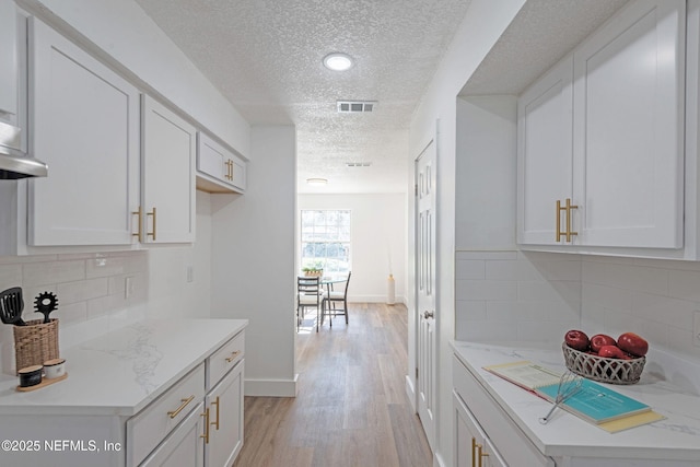 kitchen featuring light hardwood / wood-style flooring, white cabinetry, a textured ceiling, and tasteful backsplash