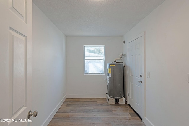 laundry room featuring water heater, light hardwood / wood-style flooring, and a textured ceiling