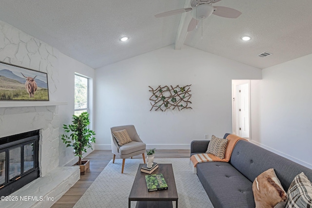 living room with a high end fireplace, a textured ceiling, ceiling fan, lofted ceiling with beams, and hardwood / wood-style floors