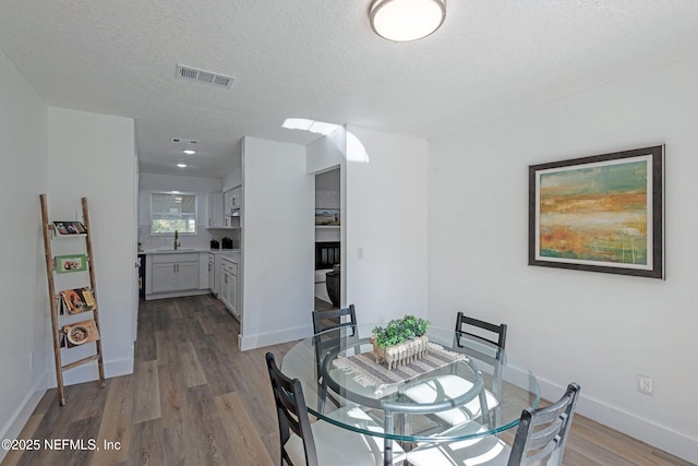 dining area with a textured ceiling, sink, and light hardwood / wood-style flooring