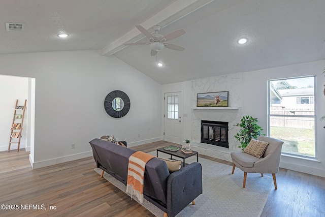 living room with a fireplace, ceiling fan, hardwood / wood-style floors, and lofted ceiling with beams