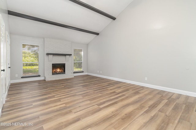 unfurnished living room featuring a fireplace, beam ceiling, light hardwood / wood-style floors, and high vaulted ceiling