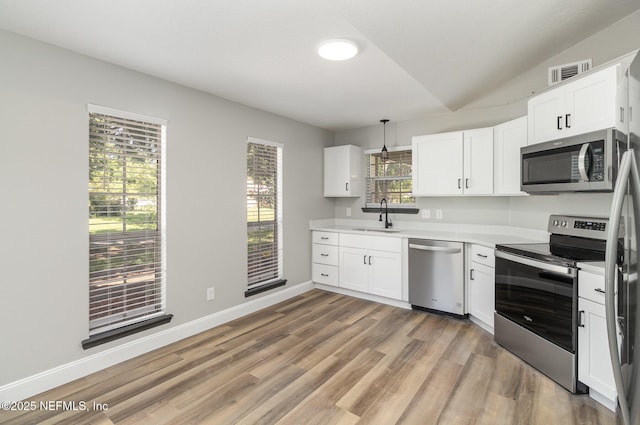 kitchen featuring stainless steel appliances, vaulted ceiling, sink, pendant lighting, and white cabinets