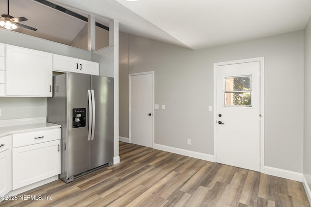 kitchen featuring ceiling fan, stainless steel fridge, wood-type flooring, vaulted ceiling, and white cabinets