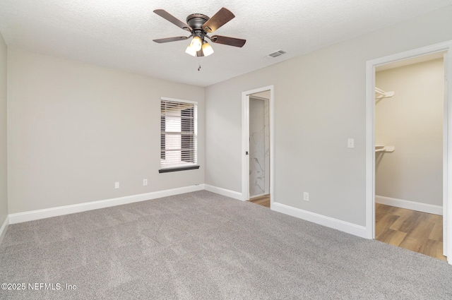 unfurnished bedroom featuring carpet, ceiling fan, a spacious closet, a textured ceiling, and a closet