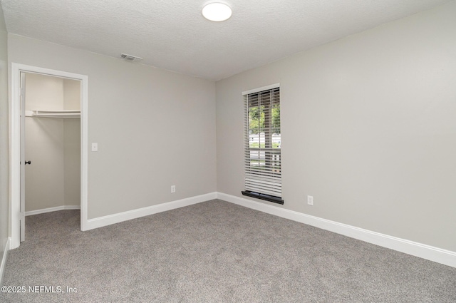 unfurnished bedroom with carpet flooring, a walk in closet, a closet, and a textured ceiling