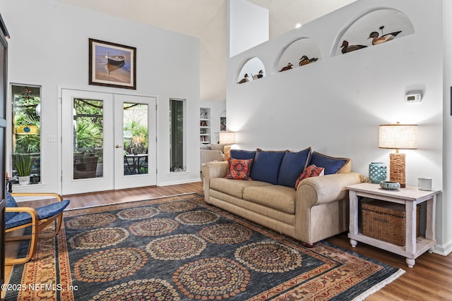 living room with french doors, a towering ceiling, built in features, and wood-type flooring