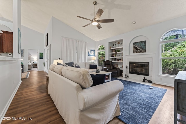 living room featuring a tile fireplace, ceiling fan, dark hardwood / wood-style flooring, built in features, and vaulted ceiling