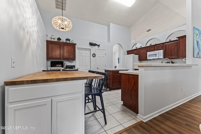 kitchen with a breakfast bar, white appliances, pendant lighting, a center island with sink, and a chandelier