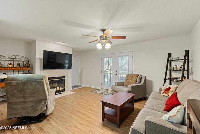 living room with ceiling fan, french doors, light hardwood / wood-style flooring, a textured ceiling, and a tiled fireplace