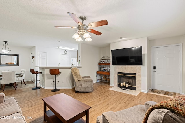 living room with a textured ceiling, light wood-type flooring, ceiling fan, and a tiled fireplace