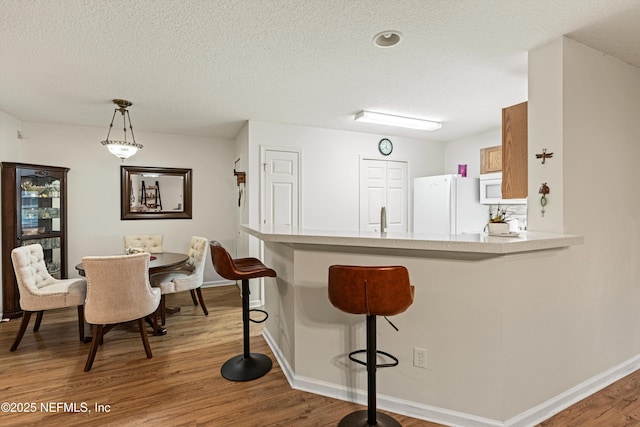 kitchen featuring kitchen peninsula, white appliances, light hardwood / wood-style floors, and hanging light fixtures