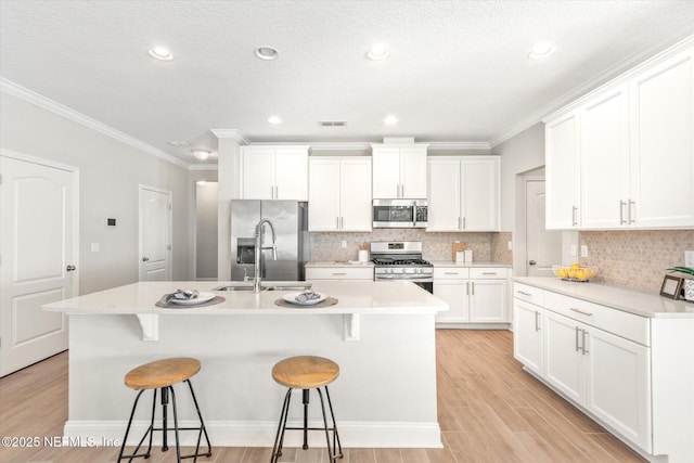 kitchen featuring stainless steel appliances, a breakfast bar, white cabinets, a center island with sink, and ornamental molding