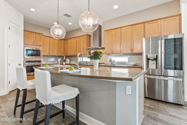 kitchen with tasteful backsplash, a kitchen island with sink, appliances with stainless steel finishes, and wall chimney exhaust hood