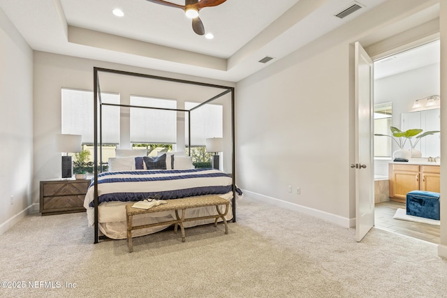 carpeted bedroom with ceiling fan, ensuite bath, sink, and a tray ceiling