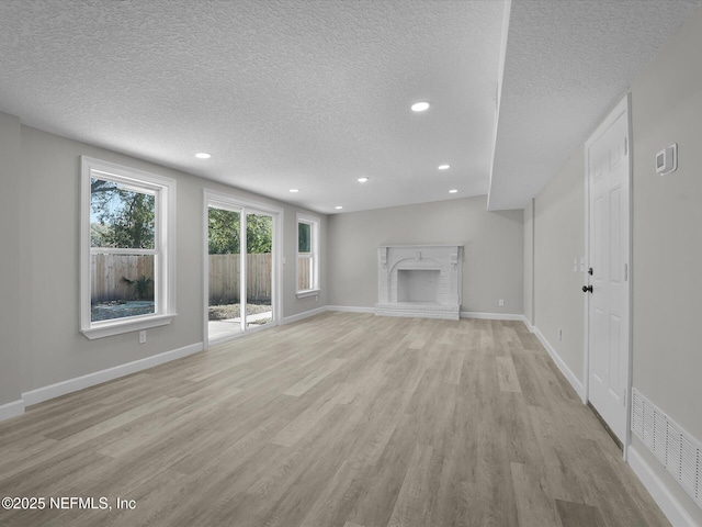 unfurnished living room with a brick fireplace, a textured ceiling, and light wood-type flooring