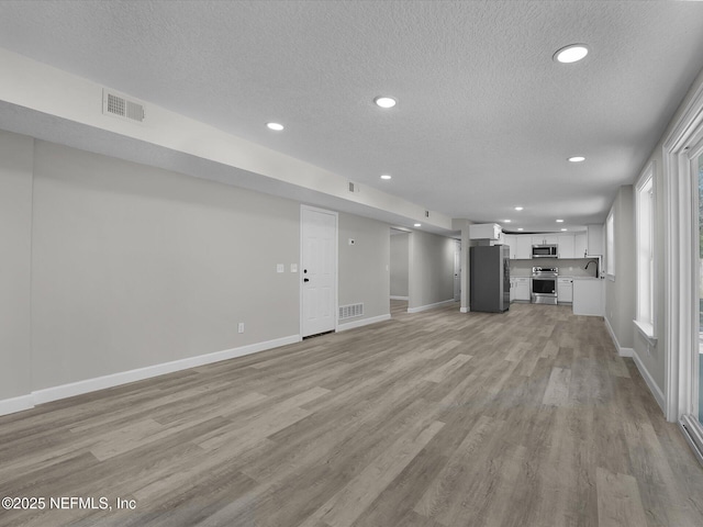 unfurnished living room featuring light hardwood / wood-style flooring, a textured ceiling, and sink