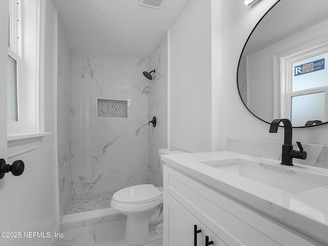 bathroom with vanity, toilet, a tile shower, and a textured ceiling