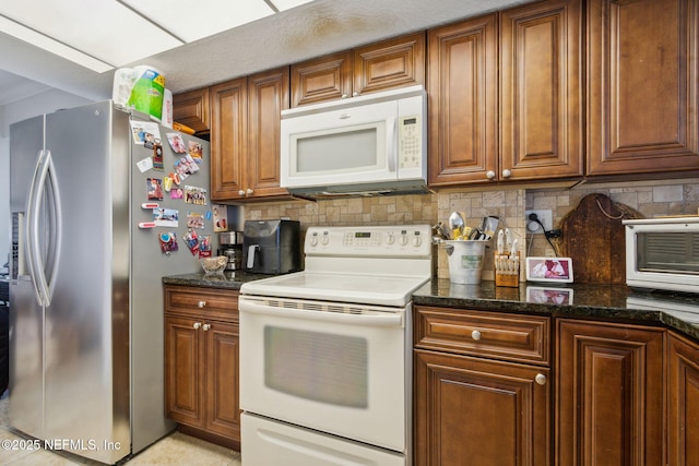 kitchen featuring white appliances, tasteful backsplash, and dark stone counters