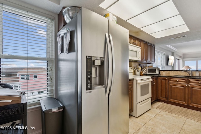 kitchen featuring sink, backsplash, dark stone countertops, white appliances, and light tile patterned floors