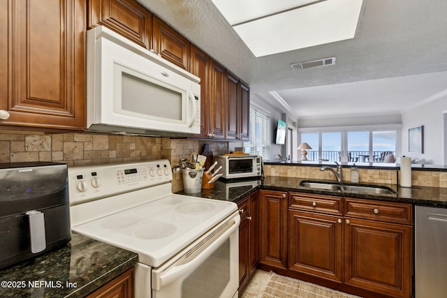 kitchen with decorative backsplash, dark stone counters, white appliances, sink, and light tile patterned flooring