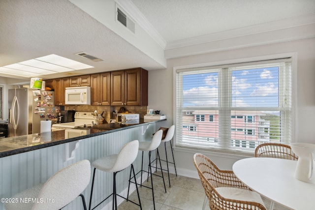 kitchen featuring white appliances, crown molding, decorative backsplash, light tile patterned floors, and kitchen peninsula