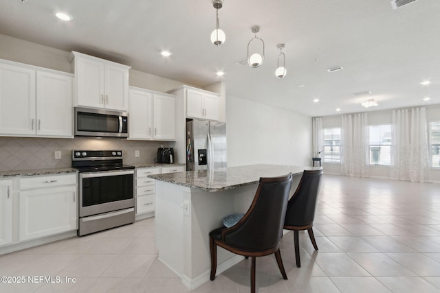 kitchen featuring light stone counters, a kitchen island, pendant lighting, and appliances with stainless steel finishes