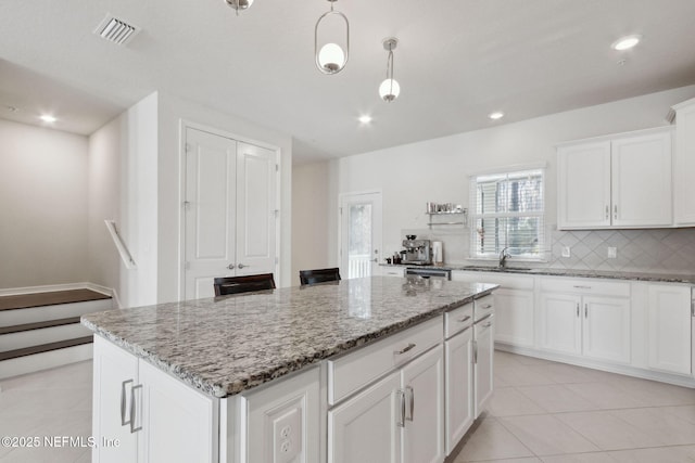 kitchen with backsplash, light stone counters, a center island, white cabinetry, and hanging light fixtures