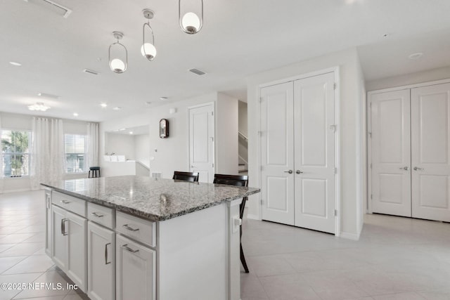 kitchen with light stone counters, light tile patterned floors, a center island, white cabinetry, and hanging light fixtures