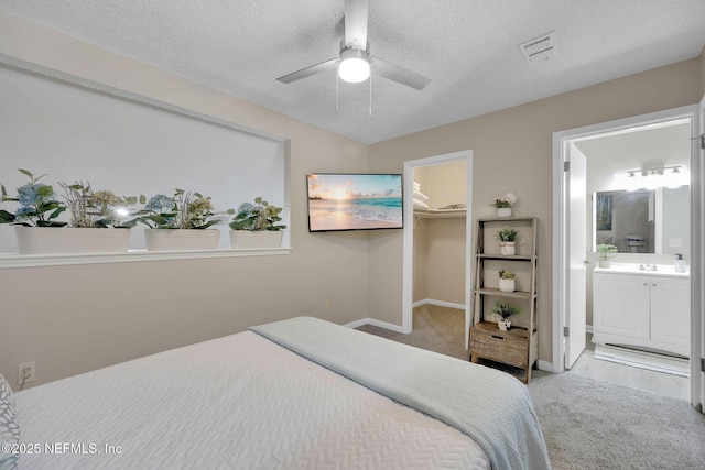 carpeted bedroom featuring ensuite bath, ceiling fan, a textured ceiling, a walk in closet, and a closet