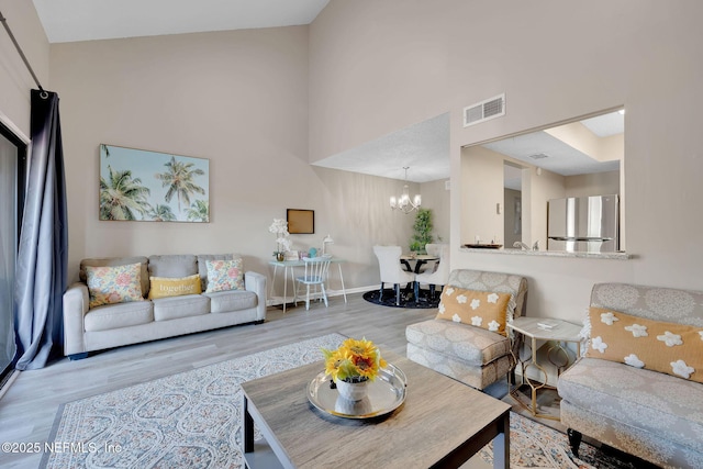 living room featuring a chandelier, a towering ceiling, and light hardwood / wood-style flooring