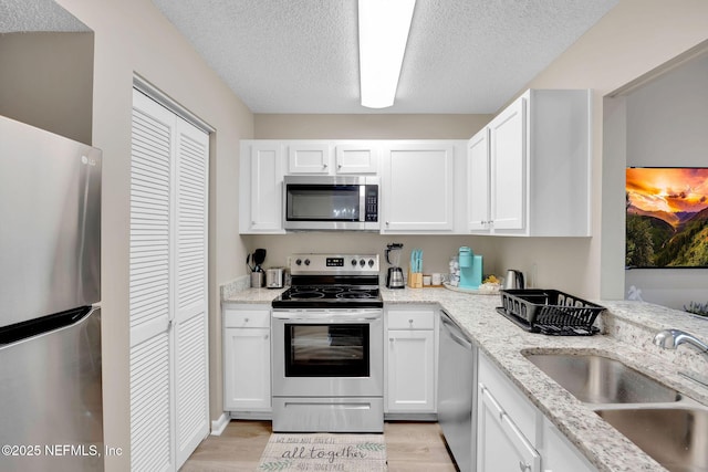 kitchen featuring white cabinets, sink, light wood-type flooring, light stone counters, and stainless steel appliances